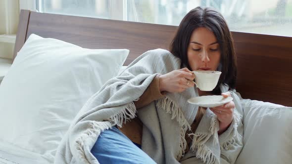 Young woman wrapped in blanket having tea 4k