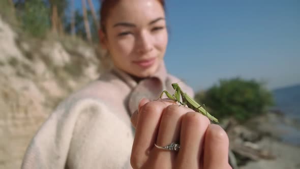 Closeup Green Mantis on Female Caucasian Hand with Blurred Young Woman Smiling at Background