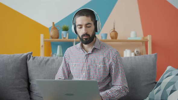 Handsome Arab Guy Working with Laptop Typing Wearing Headphones at Home