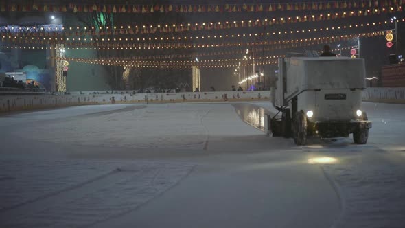 Ice Recovery and Maintenance Machine on a Skating Rink Evening Colored Lights Snowfall