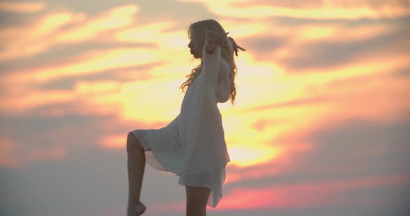 Fit Young Lady in White Dress is Dancing in the Evening During Sunset