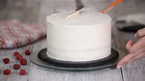 Step by step. Woman's hand spreading whipped cream on sponge cake.