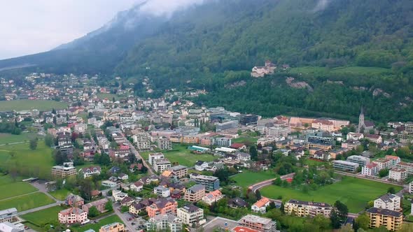 Picturesque View Of Vaduz Town Nestled In The Foothills Of Dense Mountains In Liechtenstein. Aerial