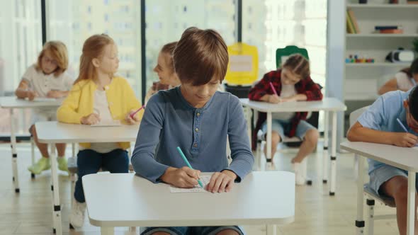 Male Pupil Sits at a First Desk in the Classroom and Fills Out Tests Thinking and Writing Down