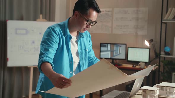 Asian Man Engineer With A Laptop Looking At Blueprint While Working At The Office