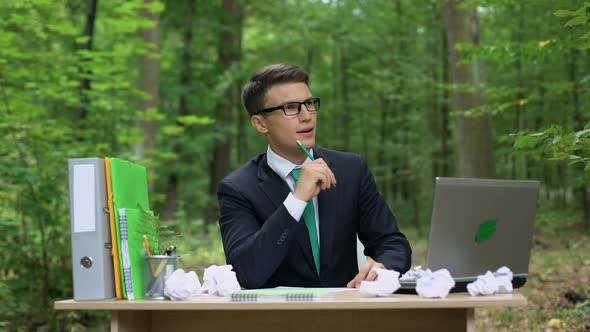 Creative Young Businessman Writing Down Good Ideas at Desk in Green Forest