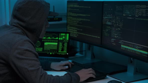 Unrecognizable man hacker wearing sweatshirt with hood typing on computer keyboard