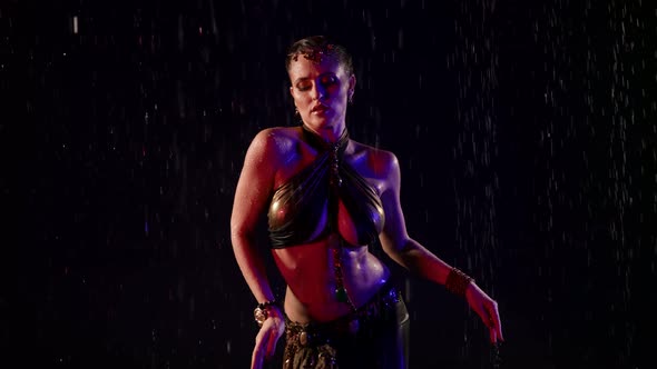 A Beautiful Woman Dances an Oriental Dance on a Black Background in the Pouring Rain in the Studio