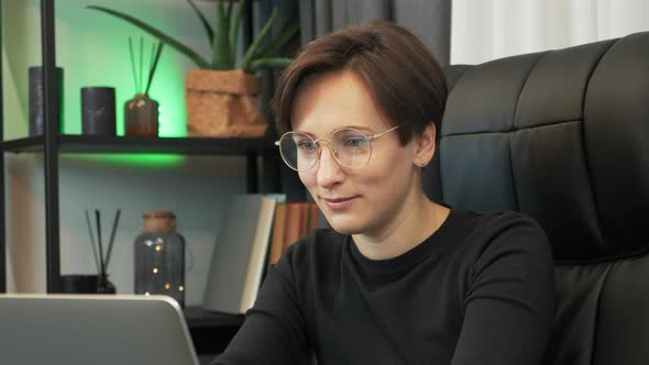 Focused smiling woman in glasses is working on laptop computer at office