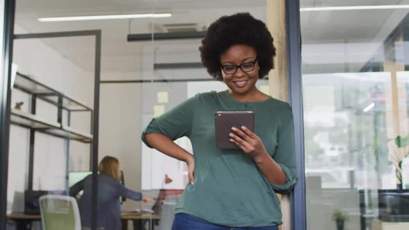 African american businesswoman leaning in doorway using tablet smiling to camera in office