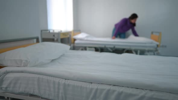 White Clean Bedding in Hospital Ward with Blurred Young Woman Making Bed at Background Leaving
