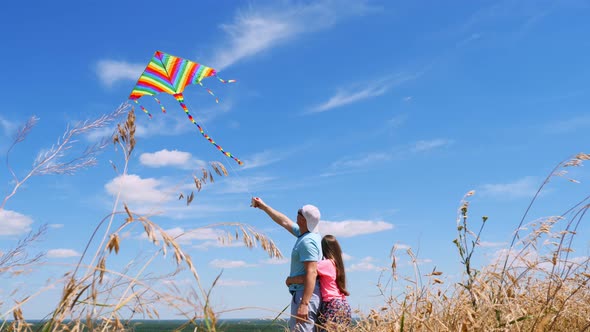 Happy Family, Dad and Daughter, Fly a Multi-colored Kite, Standing in a Field with Spikelets