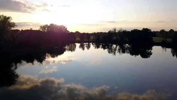 Smooth aerial drone flight slowly rise up drone shot at summer sunset on a lake at small village in