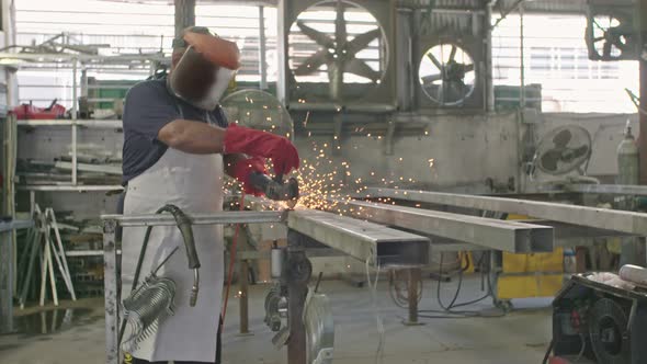 Slow motion of a worker using metal grinder with sparks flying at a metal shop