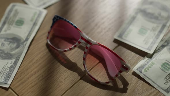 Closeup Stars and Stripes Sunglasses on Wooden Table with Dollars Falling