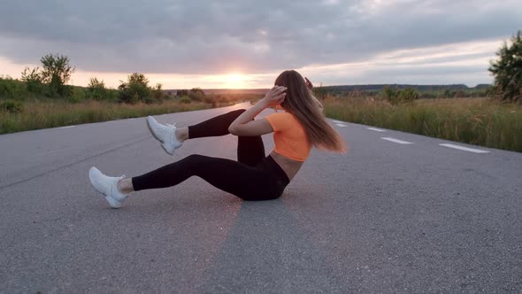 Young Athletic Girl Doing Abs Exercises Flexing Legs on Road at Nature