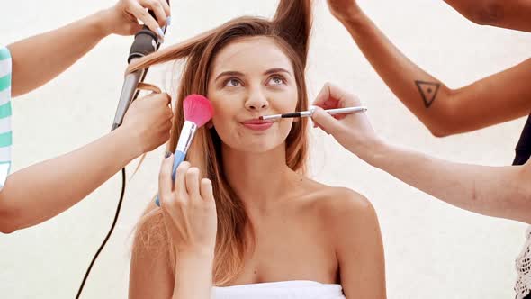 Hands Doing Hairstyle and Make Up for Young Beautiful Naked Girl in Towel Over White Background