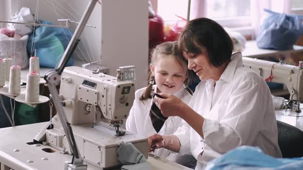 Grandma with Little Granddaughter Sew Clothes in the Factory