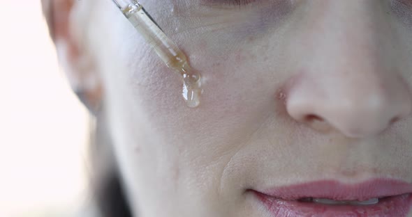 Woman Digs Face with Transparent Oil to Moisturize Skin