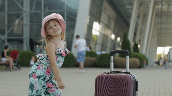 Child Girl Tourist with Suitcase Bag Near Airport. Kid Dances, Rejoices, Celebrates with Luggage