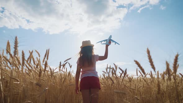 Cute Girl Playing with Toy Airplane in the Wheat Field at Sunset. Silhouette of Child Playing with