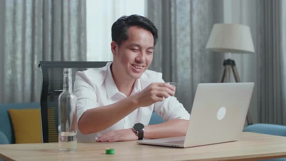 Asian Man Cheering And Drinking Vodka During Having Video Call On A Laptop At Home