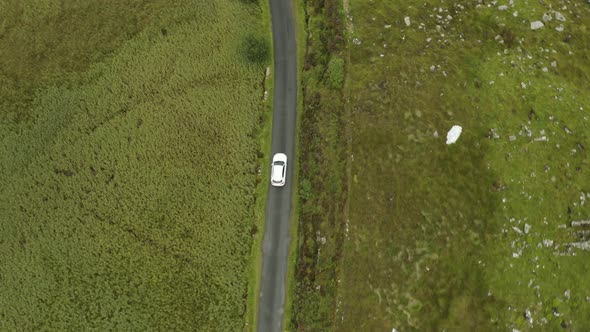 Cinematic aerial tracking shot of single white car traveling through green countryside