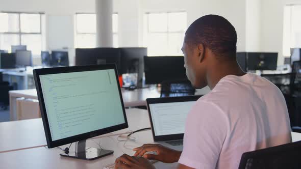 Rear view of young black male executive working desktop pc and laptop in modern office 4k