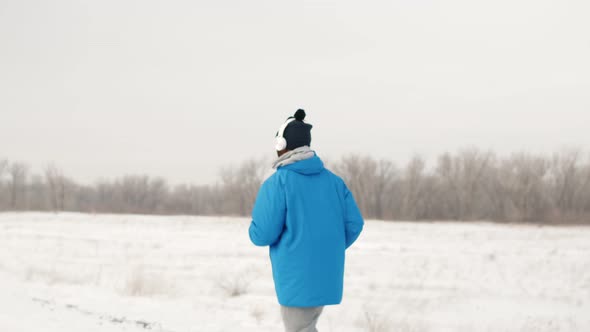 African-American man trains while jogging outside in winter with headphones and winter sportswear