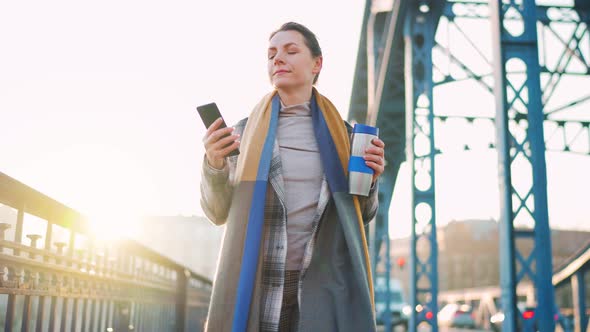 Caucasian Businesswoman in a Coat Walking Across the Bridge on a Frosty Morning Drinking Coffee and