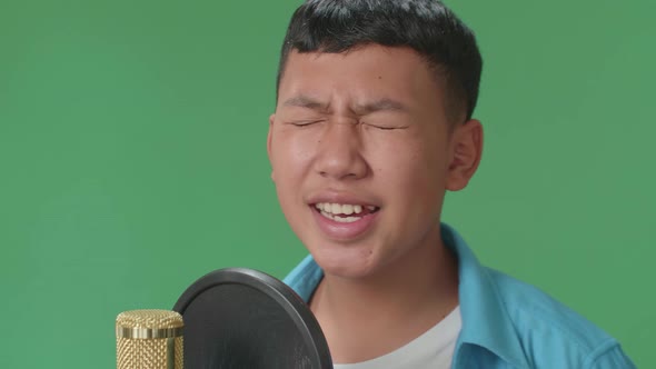 Side View Of Young Asian Boy Singing Into Microphone In Green Screen Studio