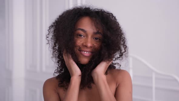 Beautiful Black Woman Looks at Camera Strokes Her Hair and Smiling in White Room