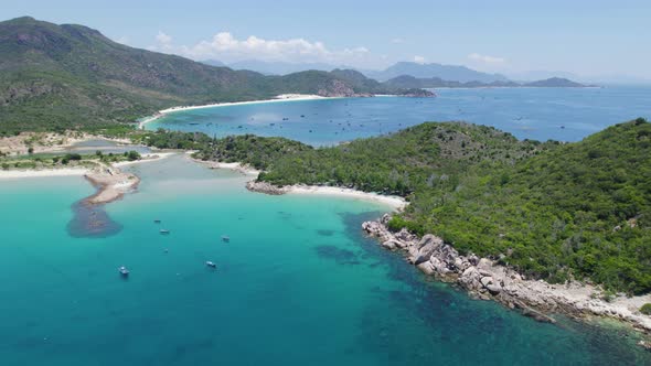 Rotating aerial over crystal clear turquoise waters at Binh Tien Beach surrounded by green cliffs in