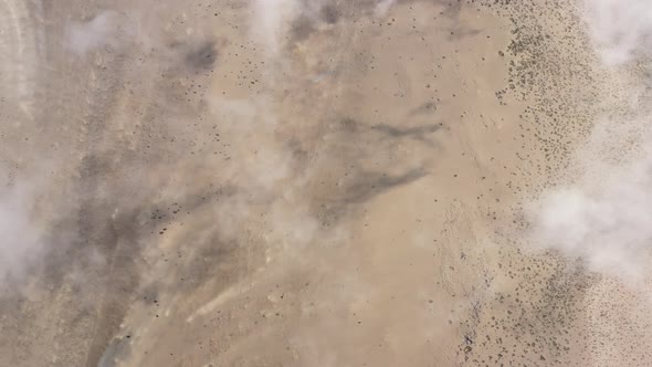 Flying above white thin clouds leaving a shadow behind on the land with brown sand and rocks