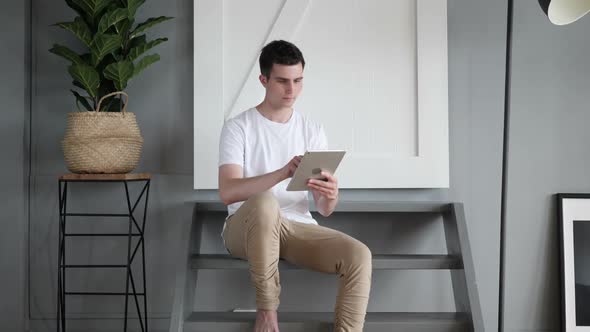 Man Sitting on Stairs Browsing and Scrolling on Tablet