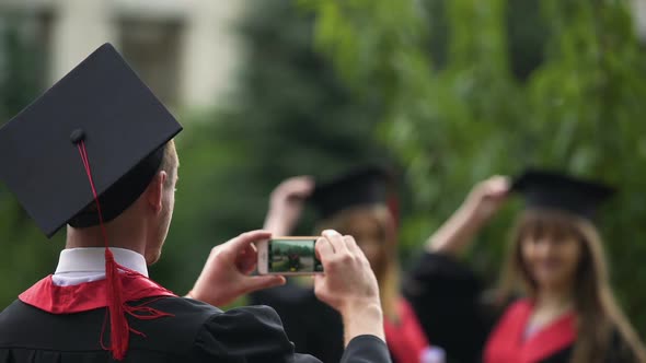 Man Filming Best Friends Throwing Graduation Caps Into Air and Posing for Camera