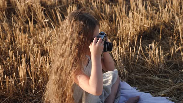 Serious Child Girl with Long Hair Sits on a Mown Wheat Field