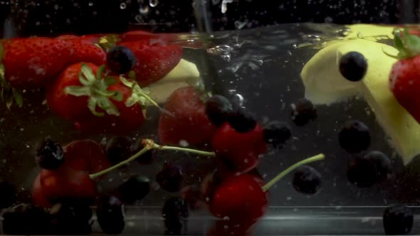 Slices of Summer Fruits Slowly Being Stirred in Transparent Liquid