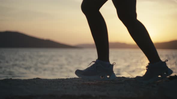 Women's Legs in Sneakers Run on the Rocks By the Ocean at Sunset