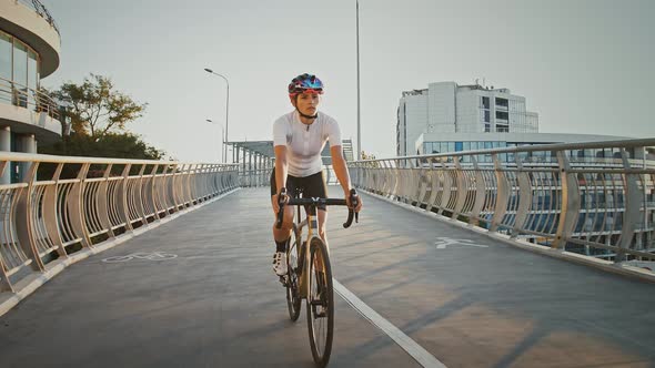 Woman in Sportswear and Protective Helmet is Riding a Sports Bike Along Bridge Surrounded By Modern