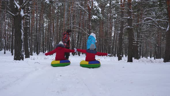 Happy Dad and Mom Pull Sleds with Children in Winter Forest. Parents Play with Children in a Snowy Park