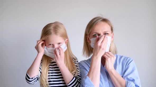 Blonde Mother and Daughter Putting on Wearing Surgical Medical Face Mask Against Infectious Disease