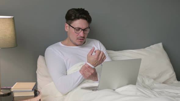 Middle Aged Man with Laptop Having Wrist Pain in Bed 