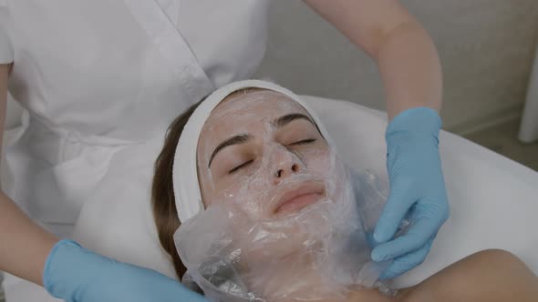 A Medical Beautician Applies a Mask to a Young Lady's Face