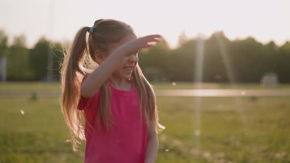 Happy Little Girl Waves Off Flying Fluffs on Spring Meadow