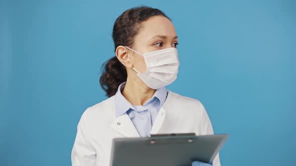 Portrait of Doctor Woman Wearing Protective Medical Mask Holding Clipboard and Looking at Camera