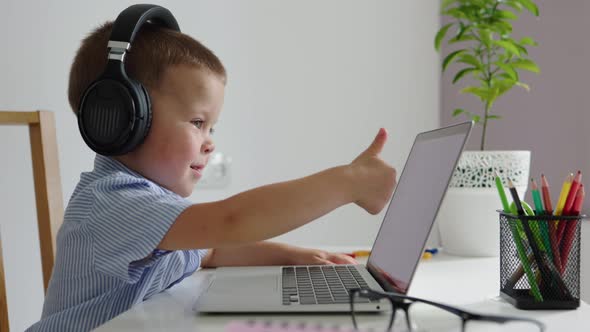 Baby Child Boy in Headphones Showing Thumb Up to Laptop Computer Screen Online alt