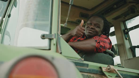 Young African Farmer Sitting in the Tractor Cabine and Showing Thumbs Up As Approval