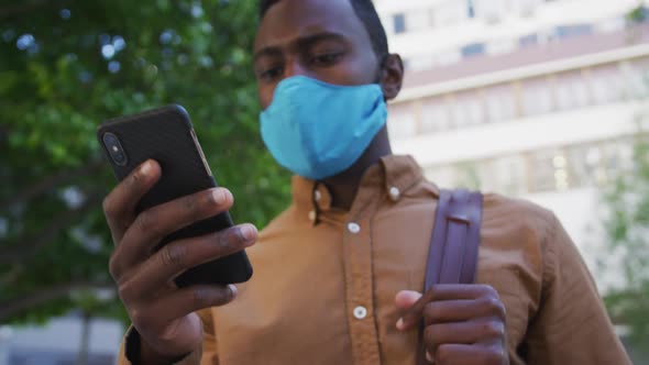 African american businessman wearing face mask using smartphone in street