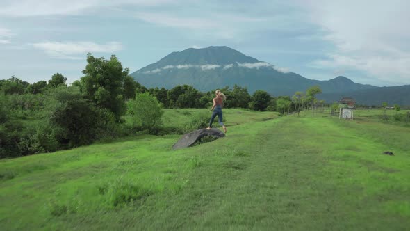 Adventure woman running barefoot on grass field steps on rock boulder celebrating with arms up, brea